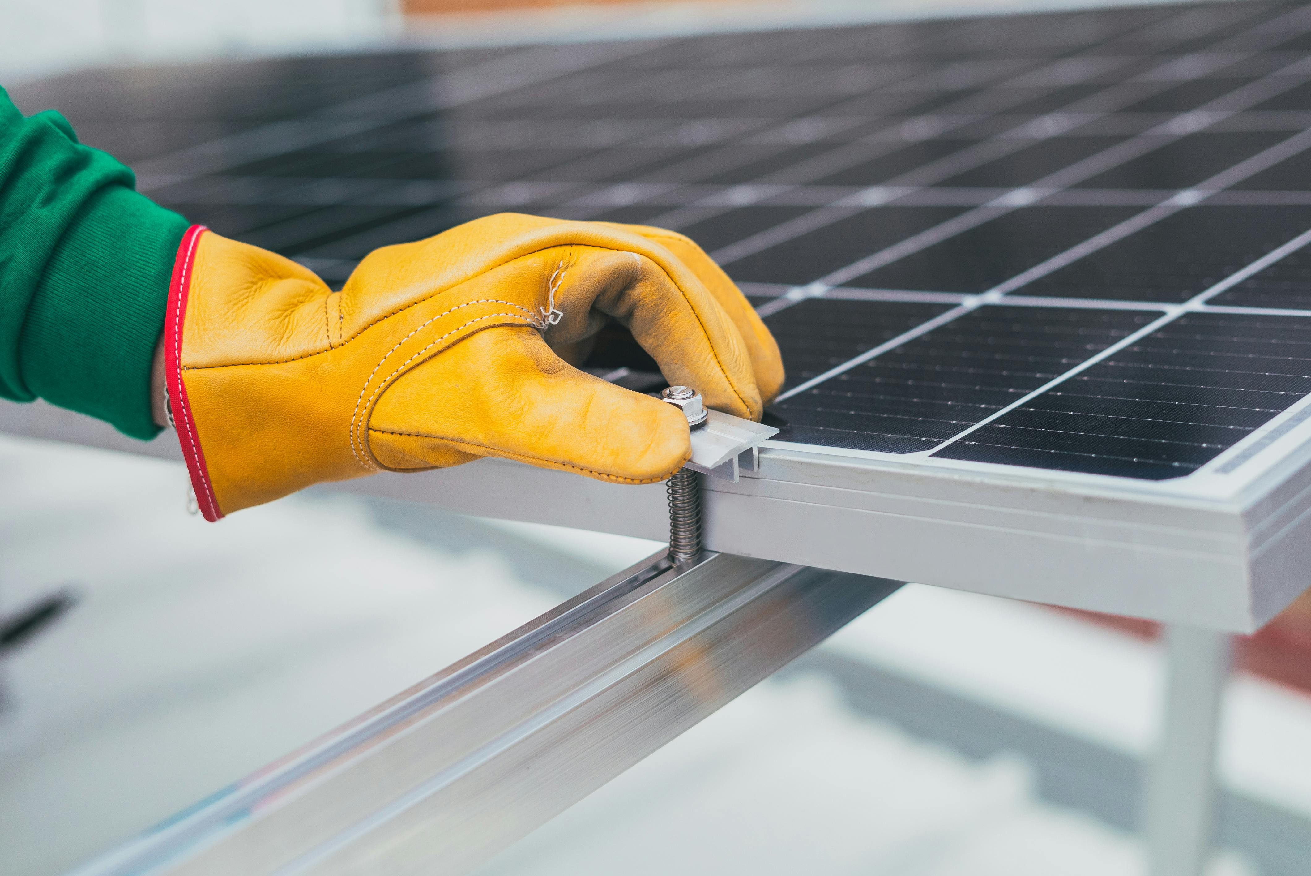 Gloved hand installing a solar panel on an aluminium bar. Photo by Los Muertos Crew on Pexels.